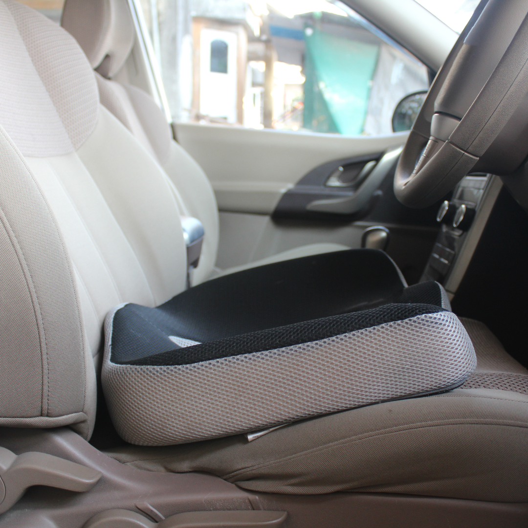 Black memory foam seat cushion placed on a car driver’s seat for enhanced lower back and spine support.